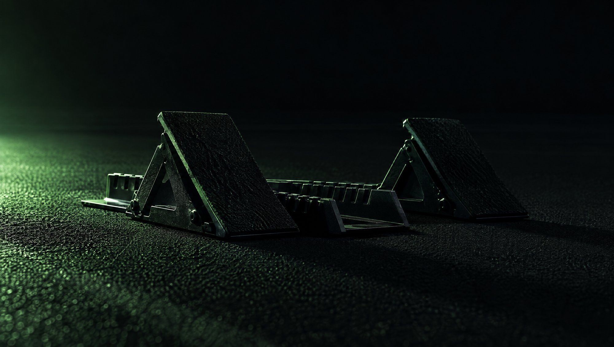 A pair of empty starting blocks on a dark running track, low angle, with green light raking across the surface.